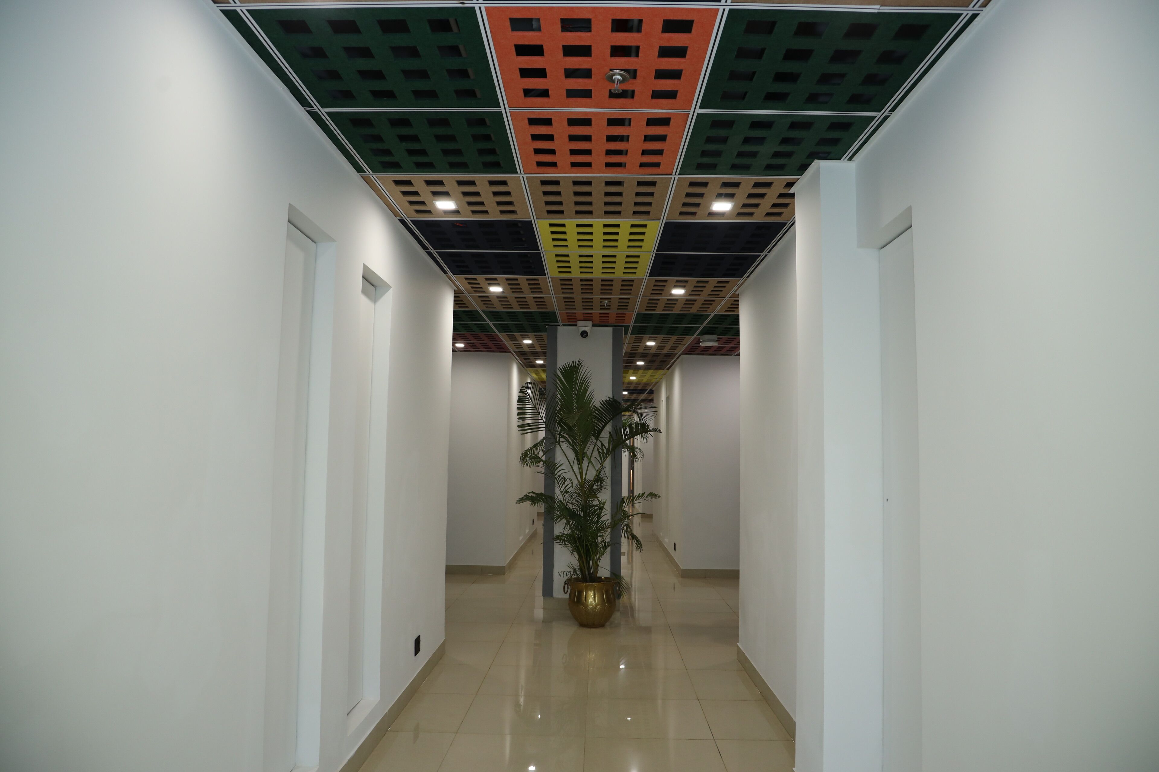A hallway with a tiled floor, white walls, and a ceiling with a grid pattern.
