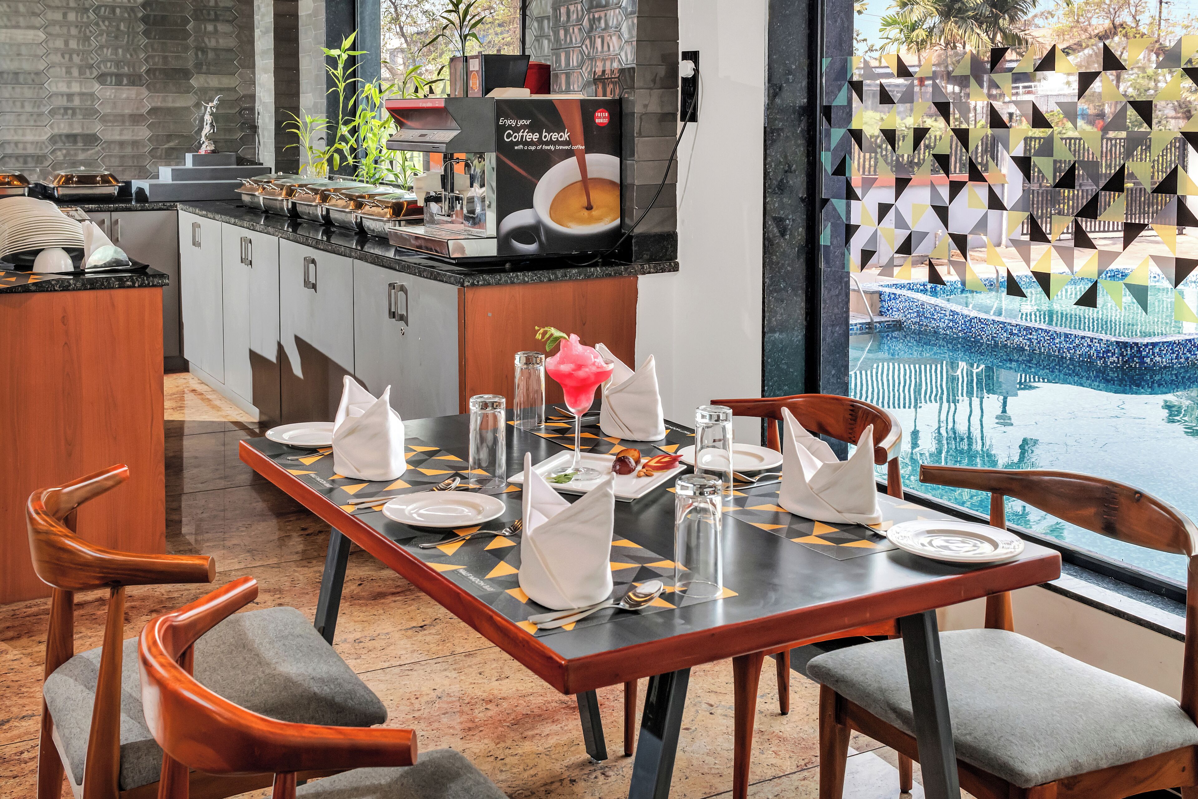 A dining area with a long table set for six, a coffee machine, and a view of a pool.