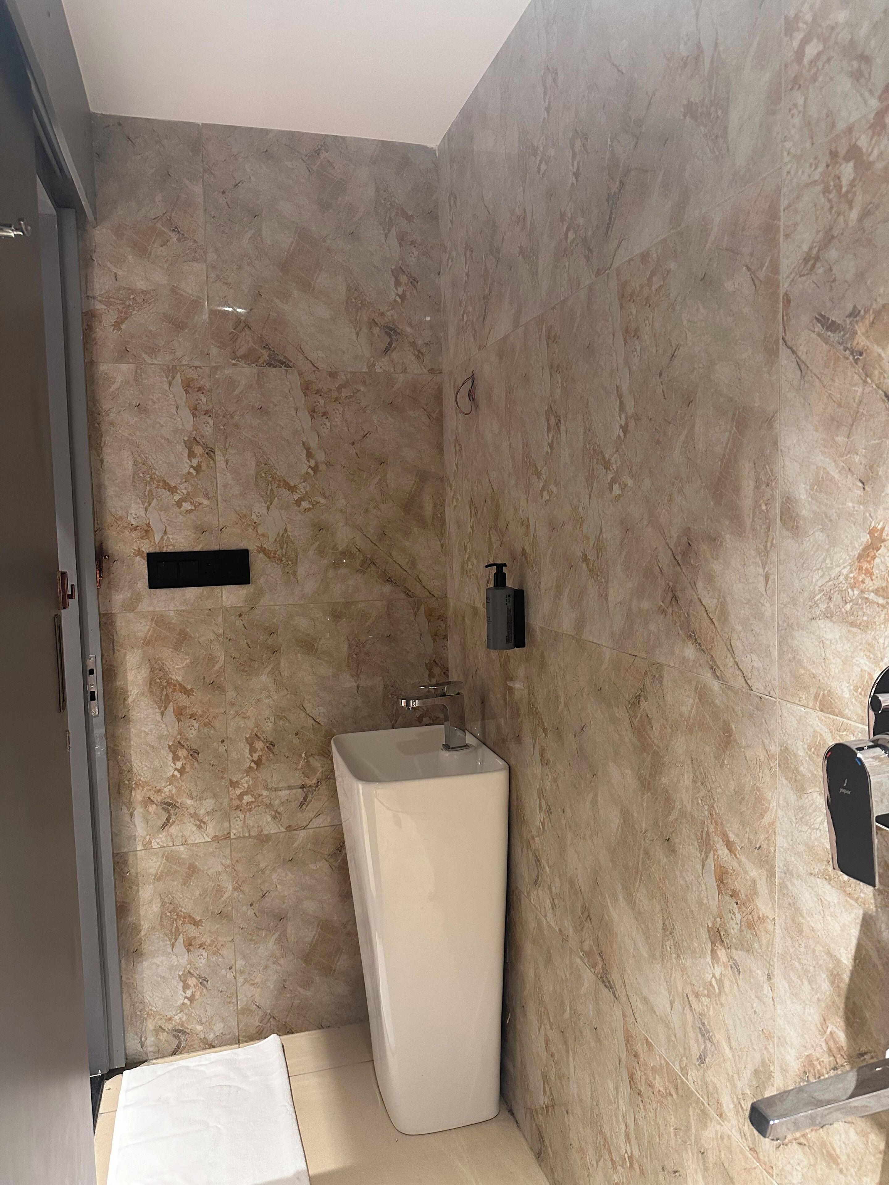Une salle de bain avec un mur en marbre, un lavabo blanc et un sèche-mains.