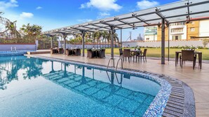 Une piscine avec un bord carrelé, un espace extérieur aménagé avec des sièges, et une zone couverte comprenant des tables et des chaises.