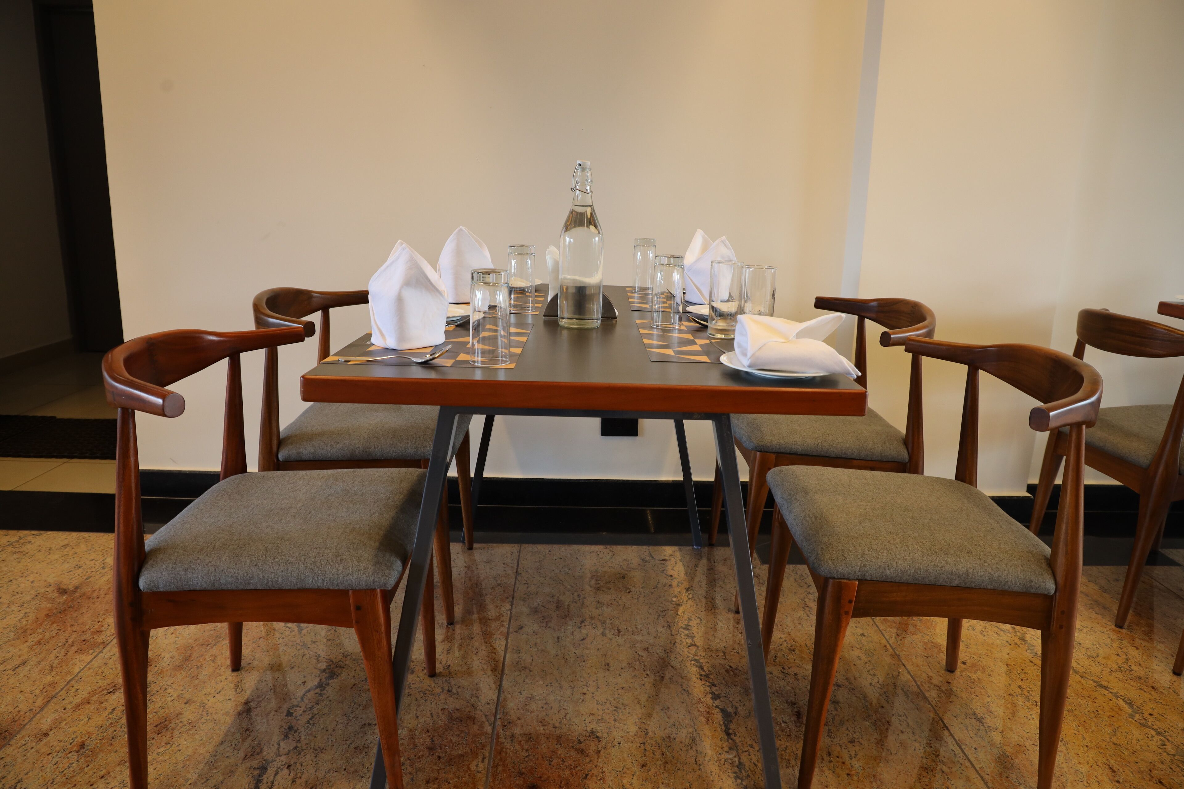 Mesa de comedor lista para seis personas, con sillas de madera, una botella y vasos.