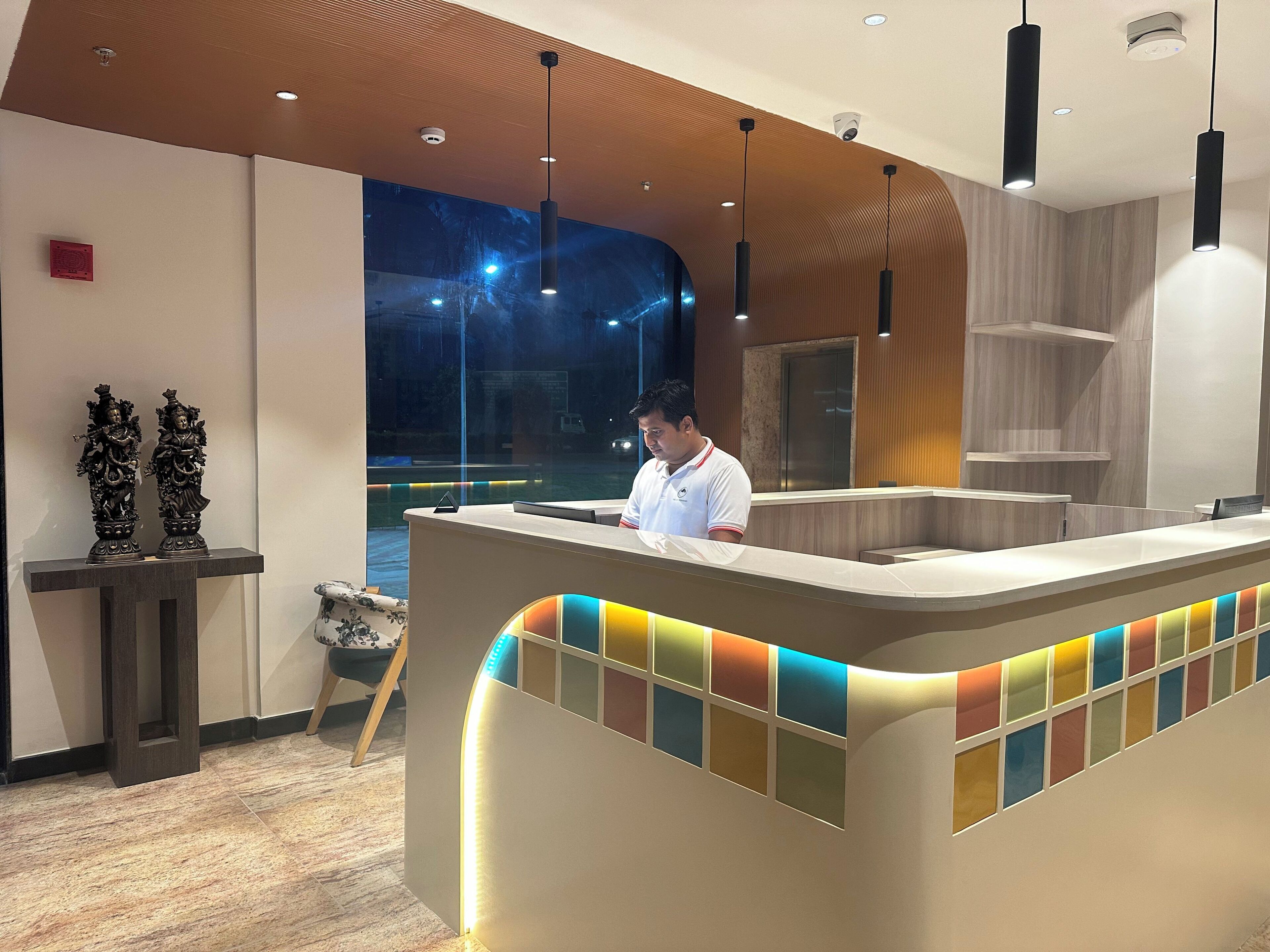 A hotel reception area with a modern design, featuring a reception desk, a large window with a view of the outside, and a decorative statue on the left.