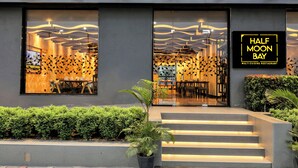 L’extérieur d’un restaurant appelé « Half Moon Bay », qui présente un design moderne, avec de grandes fenêtres, un escalier et une enseigne.