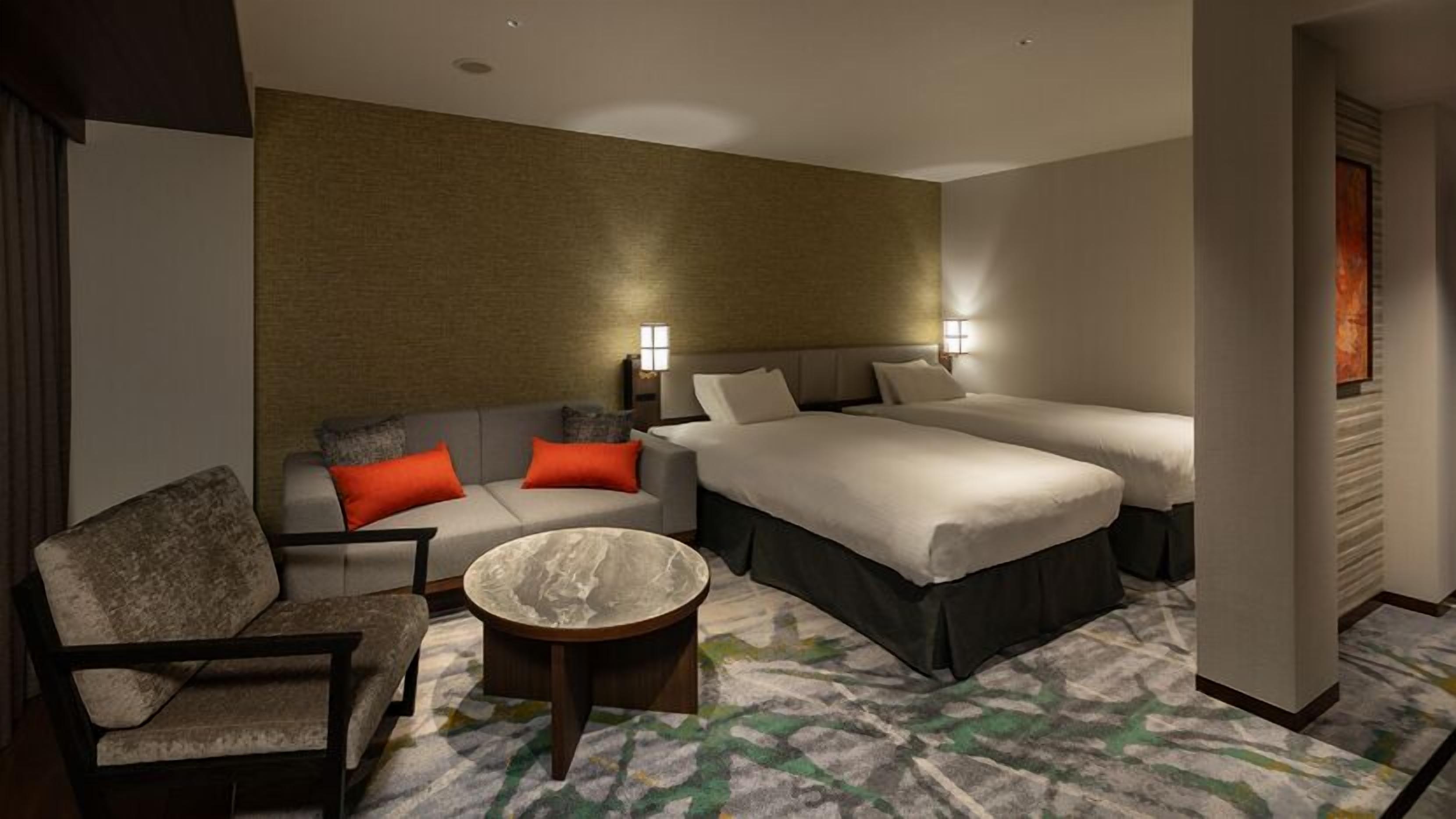 A hotel room with a sofa, two beds, a small table, and a patterned carpet.