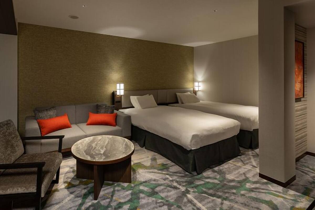 Una habitación de hotel con sofá, dos camas, una mesita y una alfombra estampada.