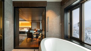 A modern bathroom with a large bathtub, a seating area with a sofa and armchairs, and a view of a snowy landscape through a large window. - EXECUTIVE SUITE SUIREI (Sapporo)
