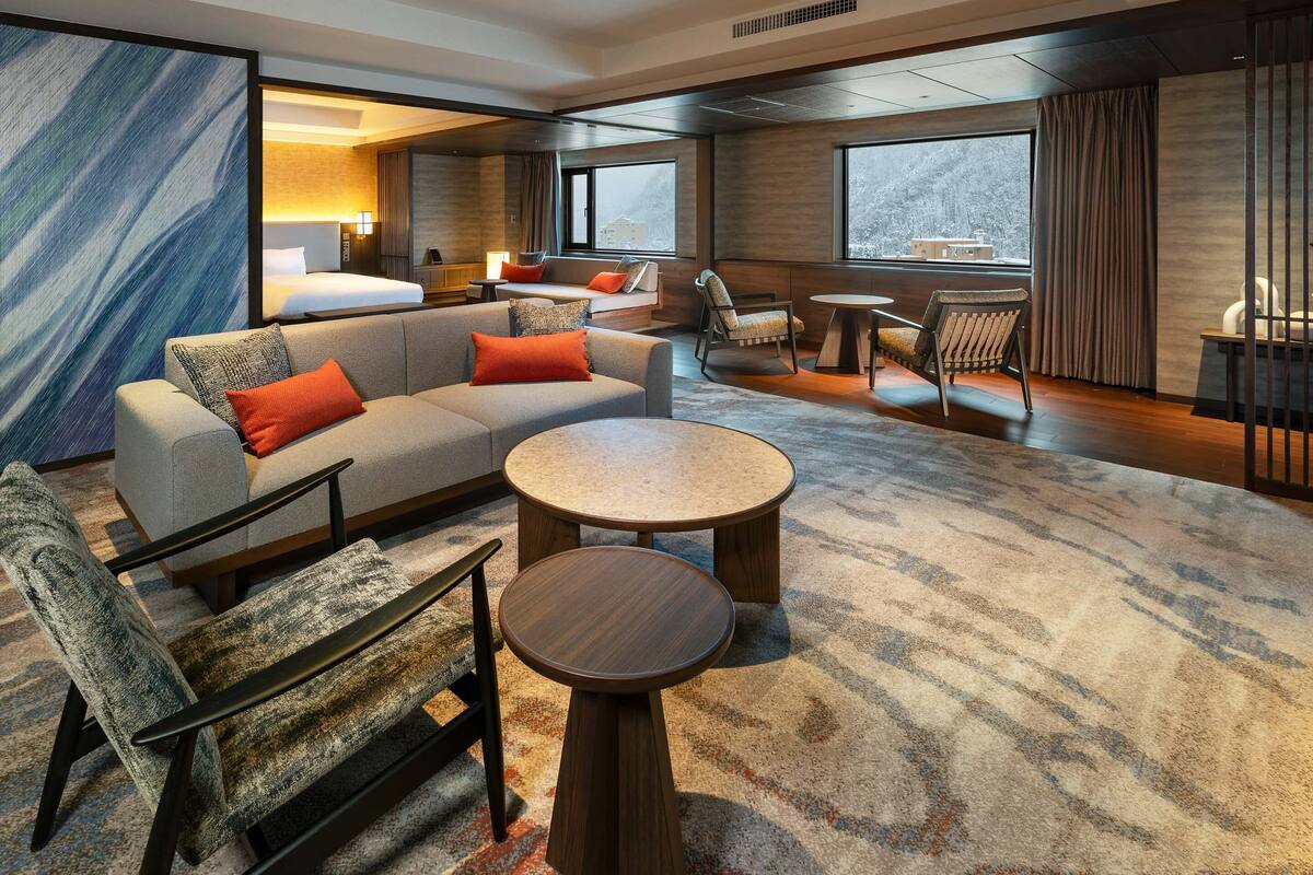 Una habitación de hotel moderna con sofá, sillones, una mesa redonda de centro y cama.