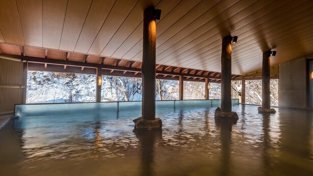 A spacious indoor area with a high ceiling and wooden beams, featuring a large open space with a view of snow-covered trees outside. - EXECUTIVE SUITE SUIREI (Sapporo)