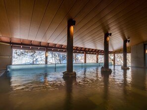 Un'ampia area interna con soffitto alto e travi in legno, caratterizzata da un grande spazio aperto con vista su alberi coperti di neve.