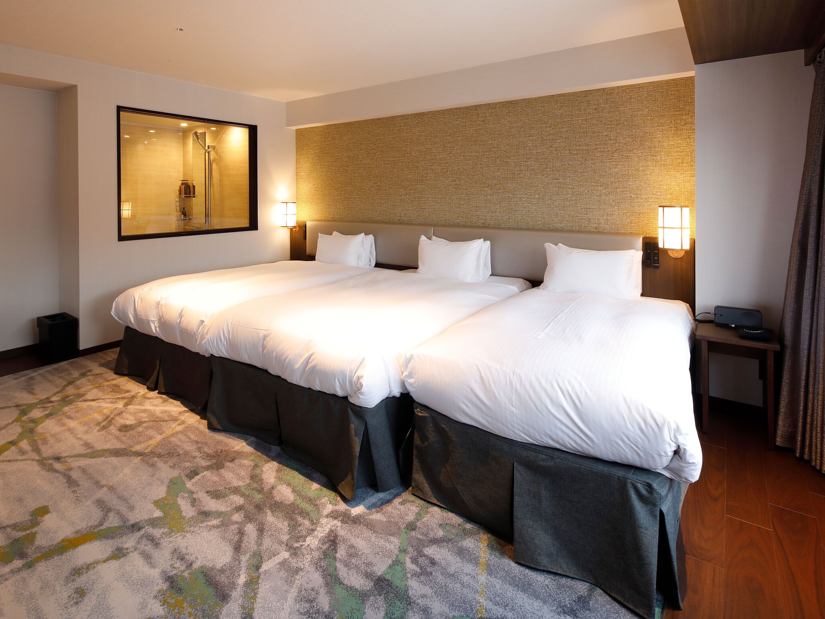A double bed with a headboard, two bedside tables, a nightstand, a mirror, and a wall-mounted lamp.