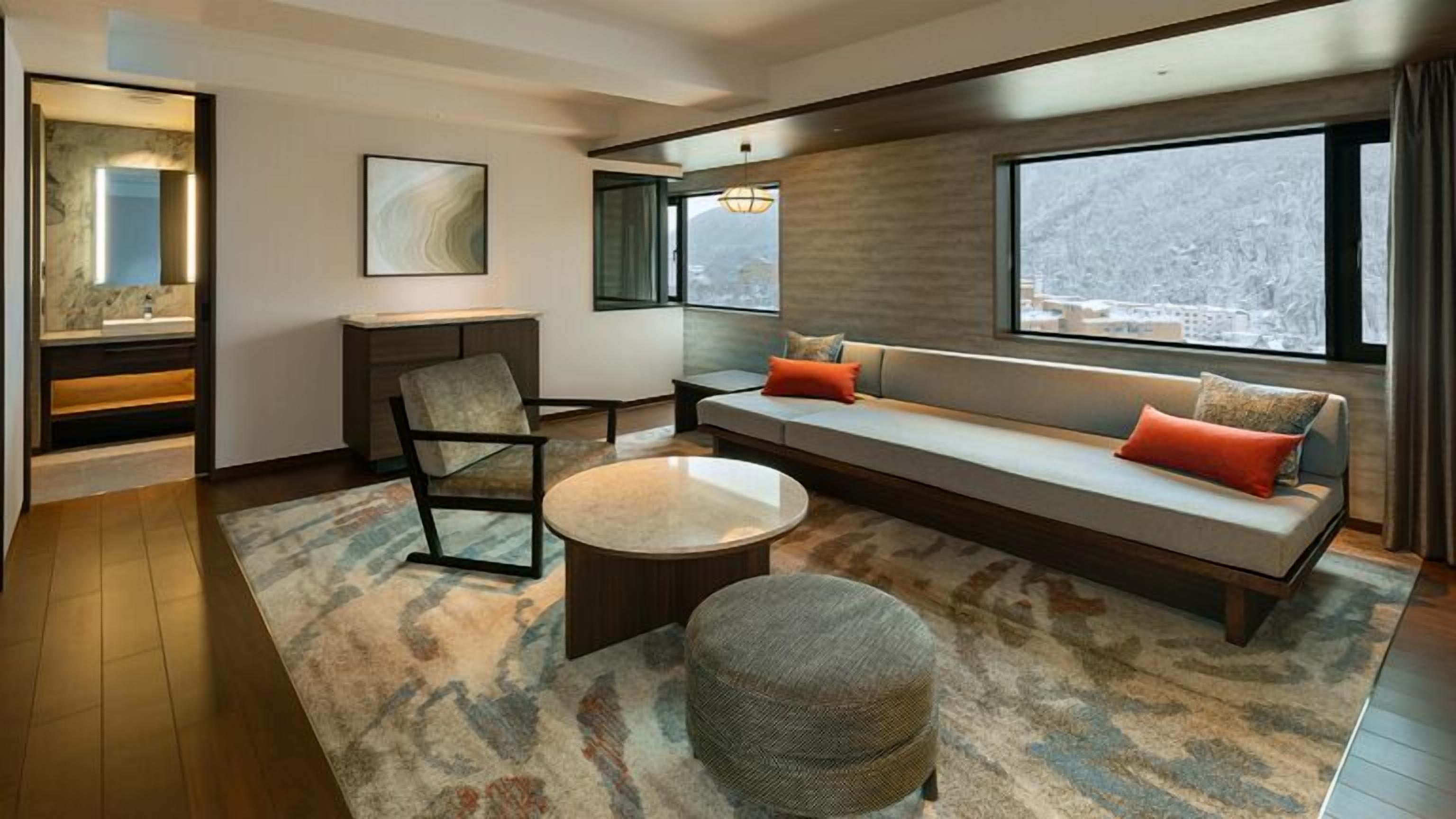 A modern living room with a sofa, armchair, coffee table, and a large window.