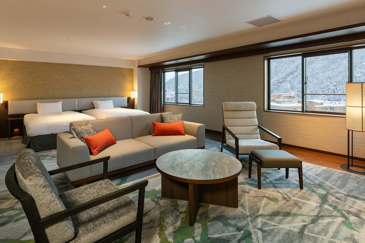 Una habitación de hotel con cama, sofá, sillón y una mesa de centro redonda.