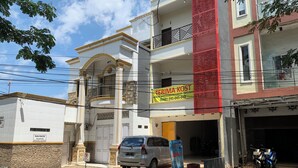 Un immeuble à plusieurs étages, doté d’une façade rouge et beige bien visible, d’un balcon apparent et d’une voiture garée devant.