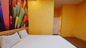Une chambre d’hôtel avec un grand lit, du linge de lit blanc et un tableau abstrait aux couleurs vives accroché au mur.