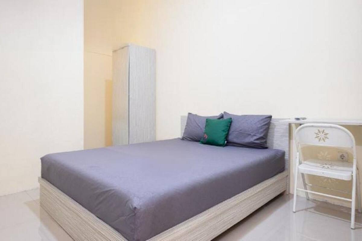 A single bed with a grey mattress and pillows, a white bedside table, and a tall wardrobe.