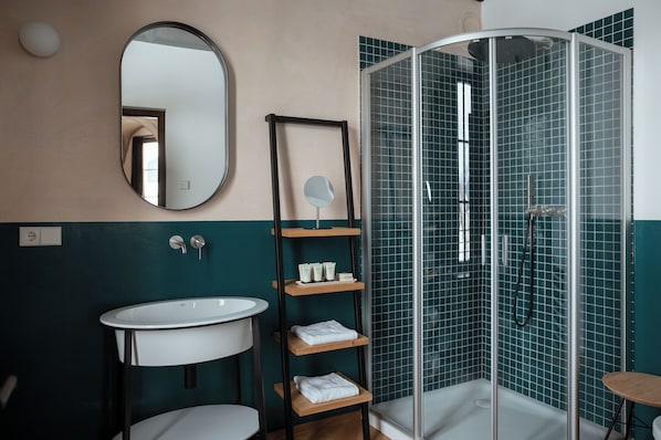 Ein Badezimmer mit einem weißen Waschbecken, einem Spiegel, einer Ablage mit Pflegeprodukten und einer Duschkabine.