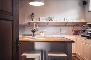 Una cocina moderna con encimera de madera, armarios blancos, una lámpara colgante y un jarrón decorativo con flores.