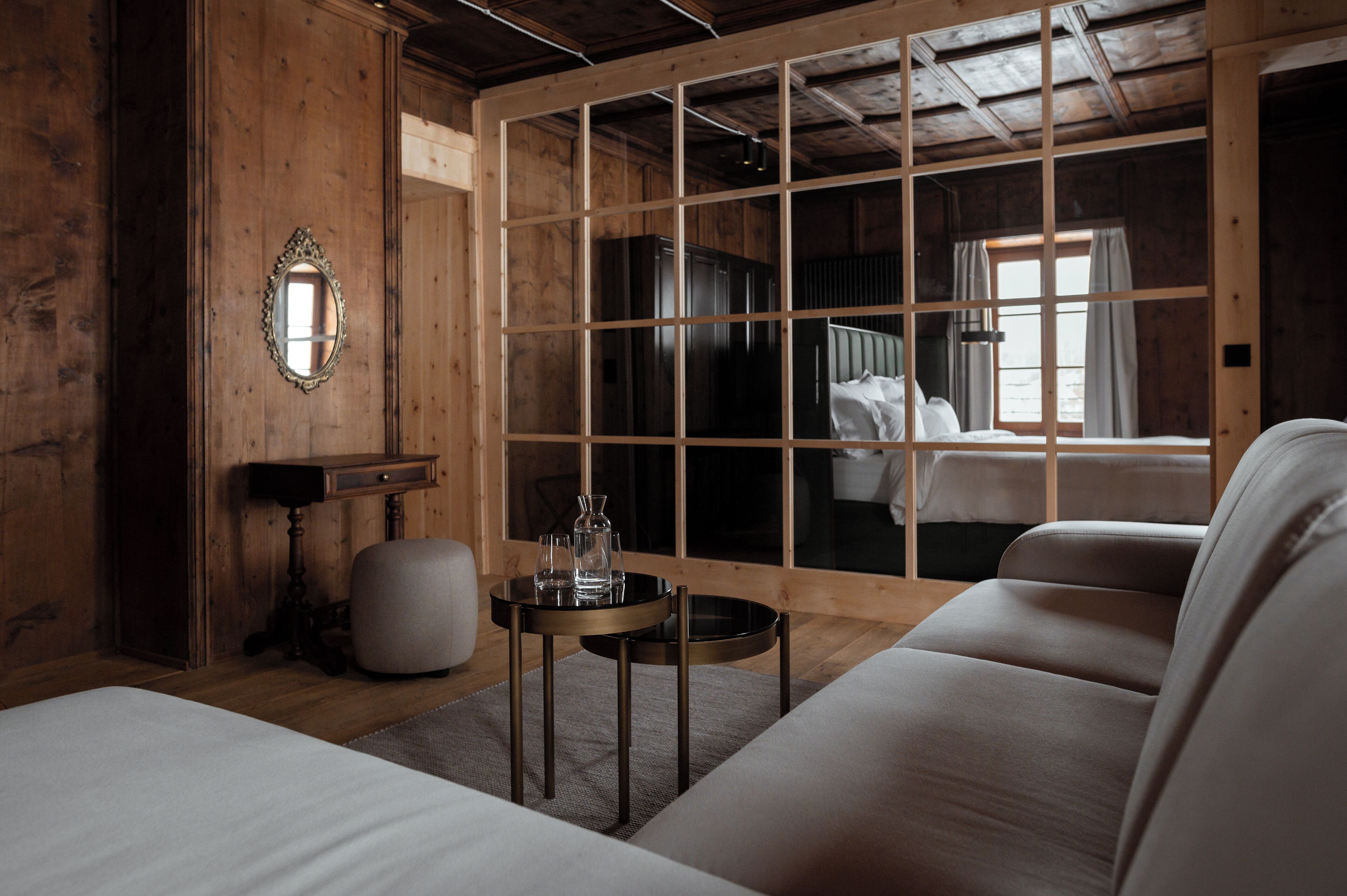 A wooden room with a bed, a sofa, a small table with glasses, and a mirror on the wall.