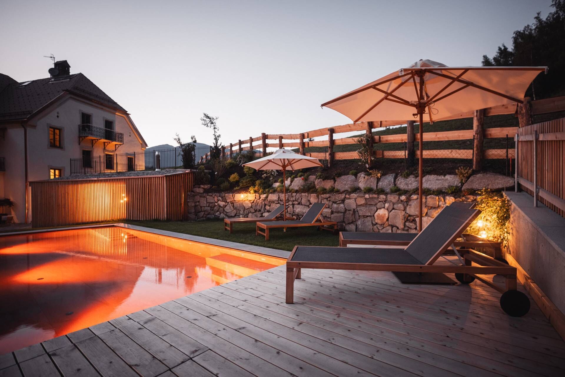Un terrazzo in legno con piscina, poltrona da relax e ombrelloni.