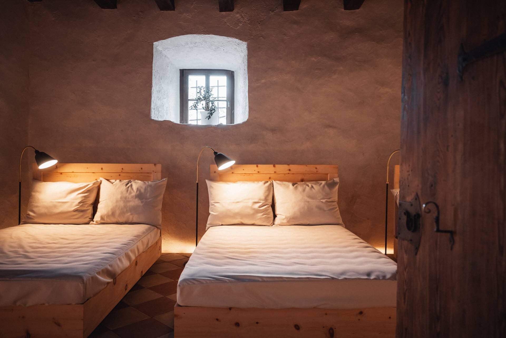 Deux lits en bois avec des têtes de lit, une petite fenêtre donnant sur un paysage agréable et une porte en bois.