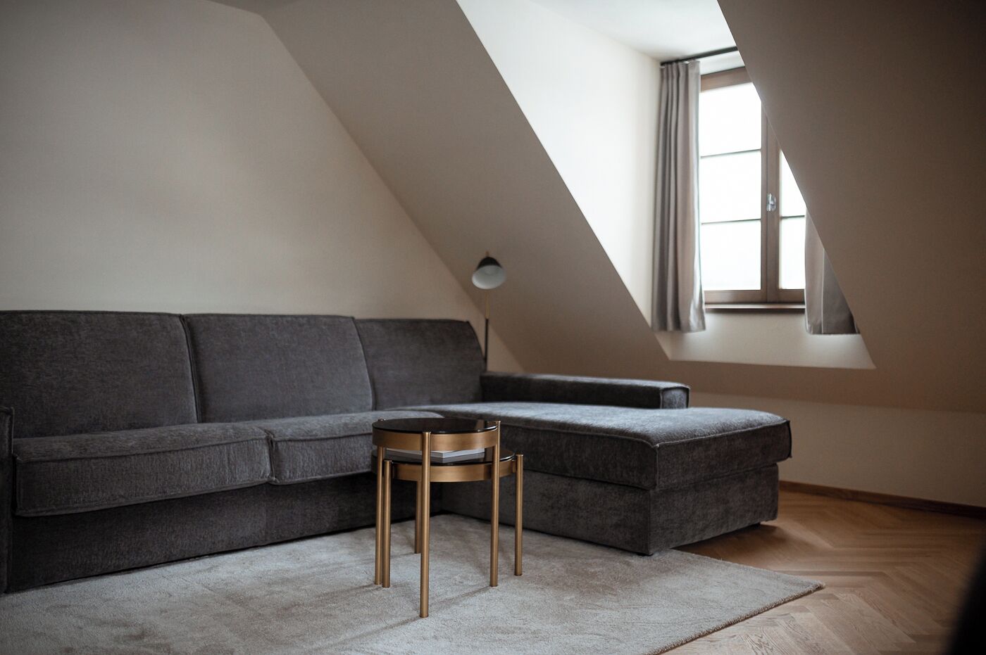 Un dormitorio tipo loft moderno con un sofá seccional gris, una mesita redonda y una ventana de tragaluz.
