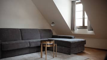 Un dormitorio tipo loft moderno con un sofá seccional gris, una mesita redonda y una ventana de tragaluz.