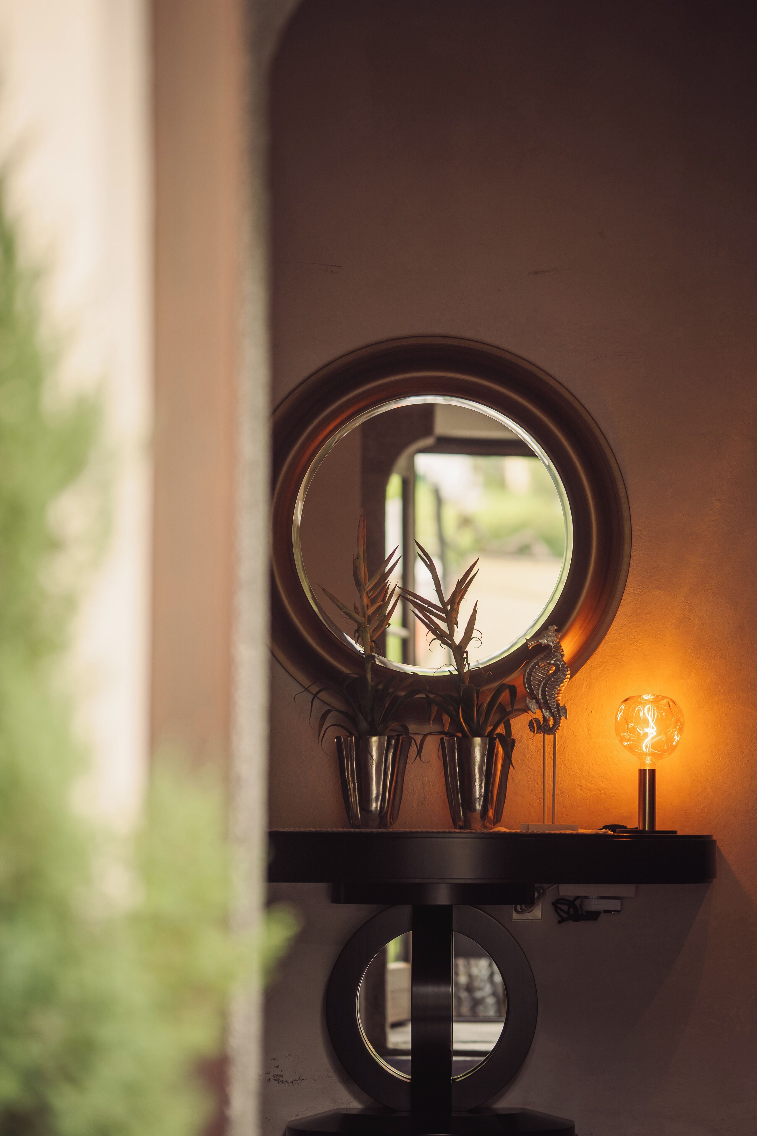 A bathroom vanity with a round mirror, a small potted plant, and a wall-mounted light fixture.
