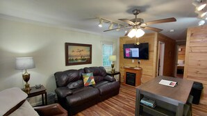 A living room with a leather sofa, a wooden coffee table, a ceiling fan, a fireplace, and a television mounted on the wall.