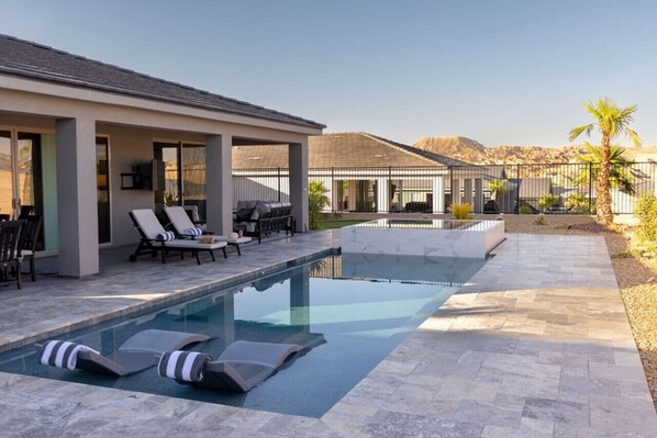 Un área de piscina moderna al aire libre con sillones de descanso, una zona de estar cubierta y vistas claras del paisaje circundante.