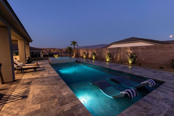 A swimming pool with lounge chairs and a covered area, surrounded by a brick wall and palm trees.