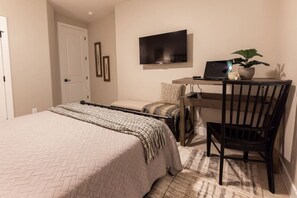 A bedroom with a bed, a desk with a laptop, a chair, a television, and a plant.