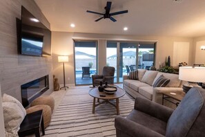 A modern living room with a flat-screen TV, a ceiling fan, a fireplace, and a large sliding glass door leading to an outdoor patio.