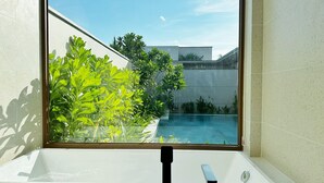 Une salle de bain moderne dotée d’une grande fenêtre donnant sur une piscine et un espace verdoyant.