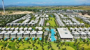 Un complexe hôtelier proposant plusieurs hébergements de type bungalow, disposés en rangées, une piscine centrale et une vue sur les montagnes lointaines.