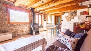A cozy cabin interior with a stone wall, wooden ceiling beams, a fireplace, a dining area, and a kitchenette. - Casa de Muntanya con Encanto (Arsèguel)