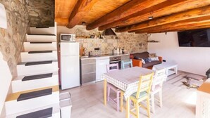 A kitchen with a stone wall, wooden ceiling beams, a microwave, and a dining area with a table and chairs. - Casa de Muntanya con Encanto (Arsèguel)