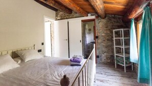 A bedroom with a wooden ceiling, a bed with white bedding, a wooden ladder, and a stone wall. - Casa de Muntanya con Encanto (Arsèguel)