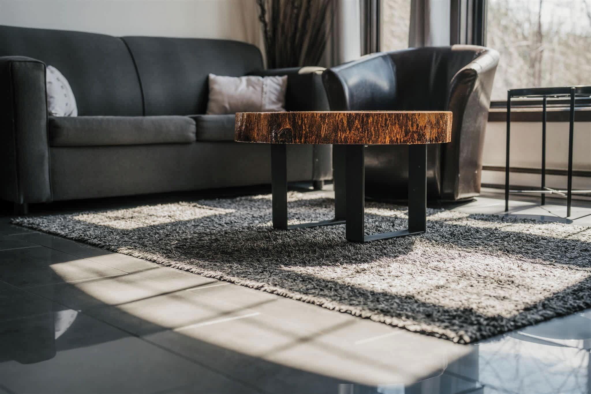 Ein modernes Wohnzimmer mit einem dunkelgrauen Ledersofa, einem Couchtisch aus Holz mit Metallbeinen und einem gemusterten Teppich.