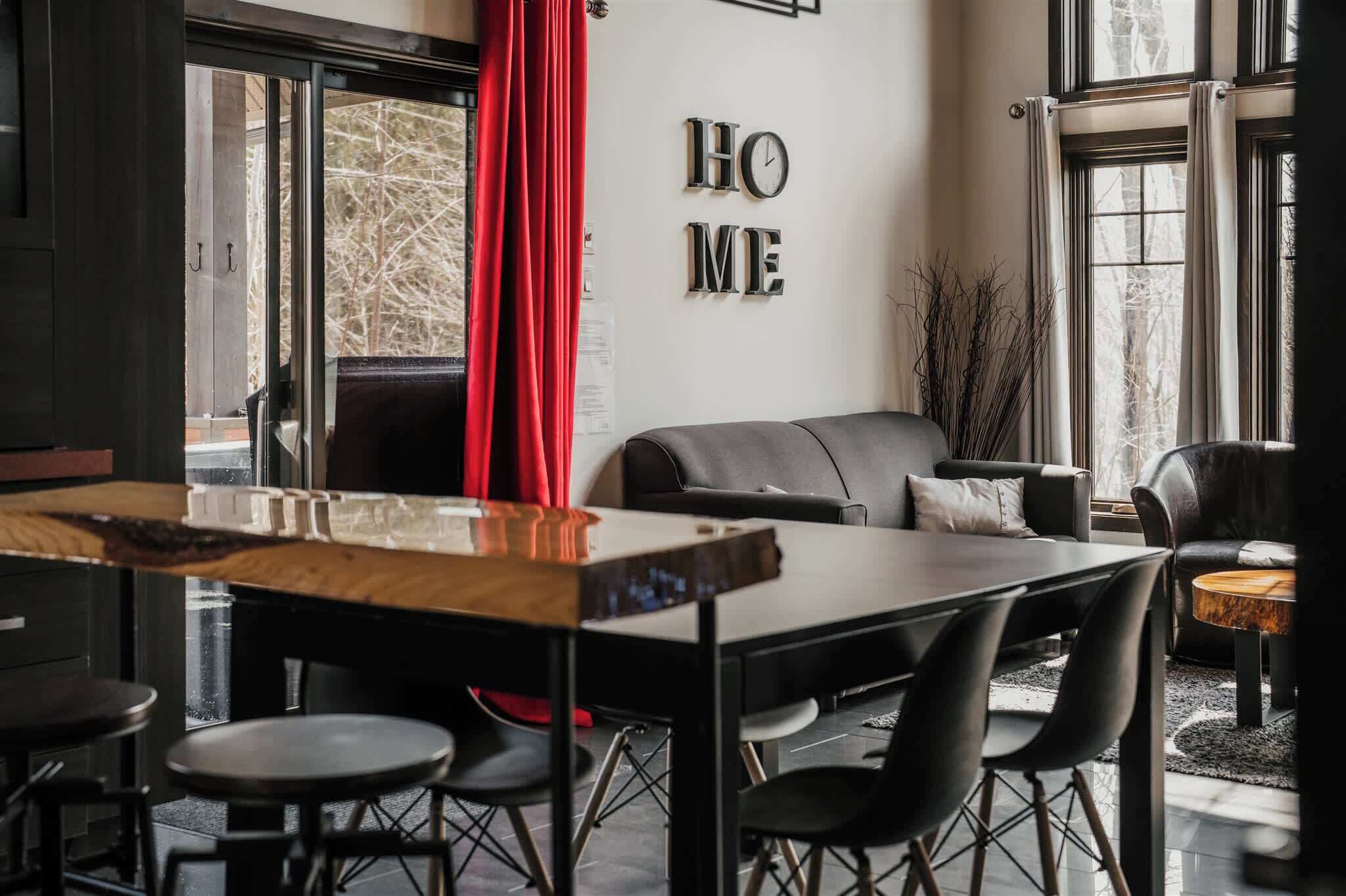 Uma sala de estar moderna com um sofá escuro, uma mesa de jantar de madeira e uma cortina vermelha.