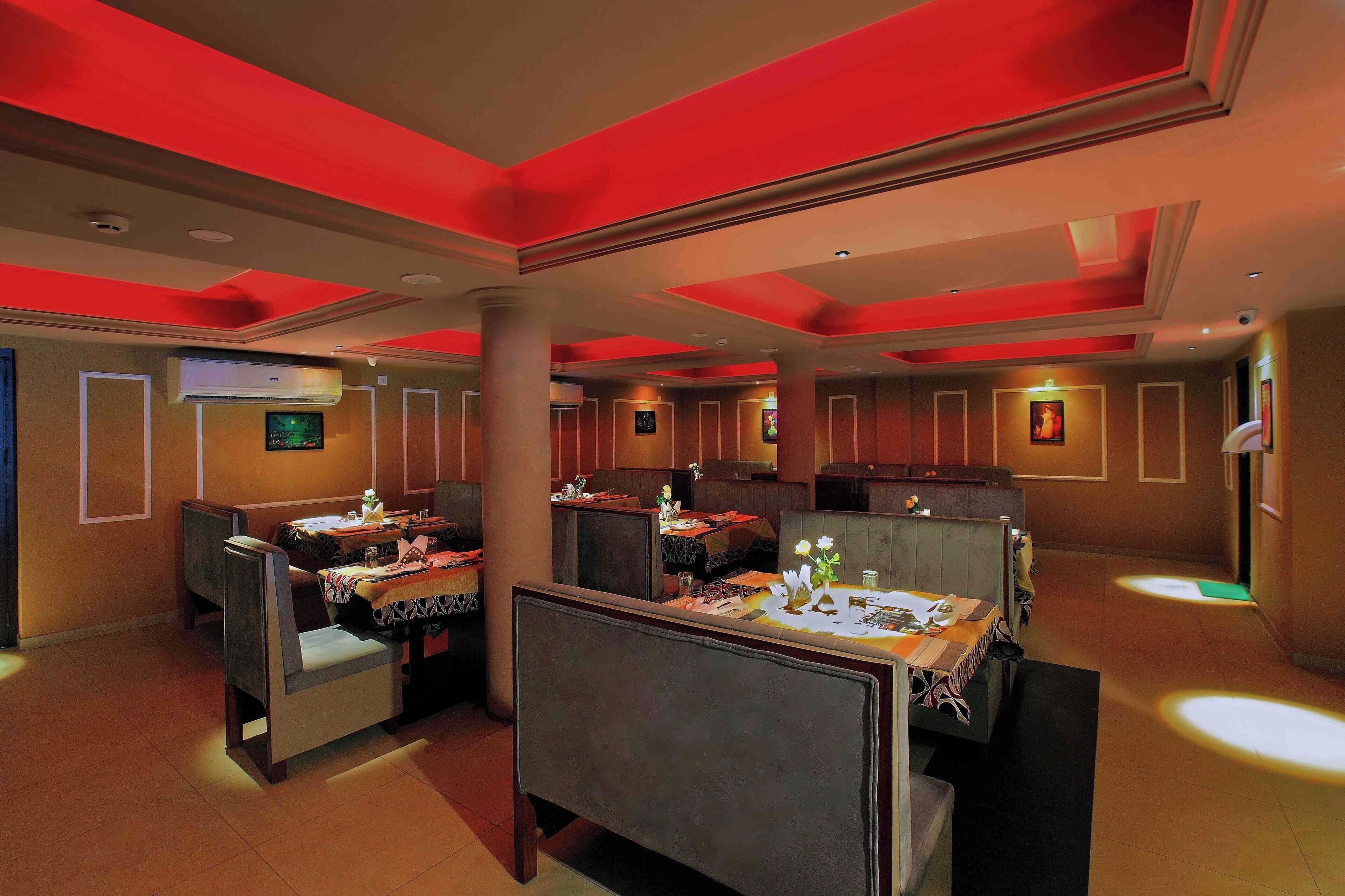 Un restaurante con cabinas y mesas altas, detalles rojos en el techo y un diseño moderno.