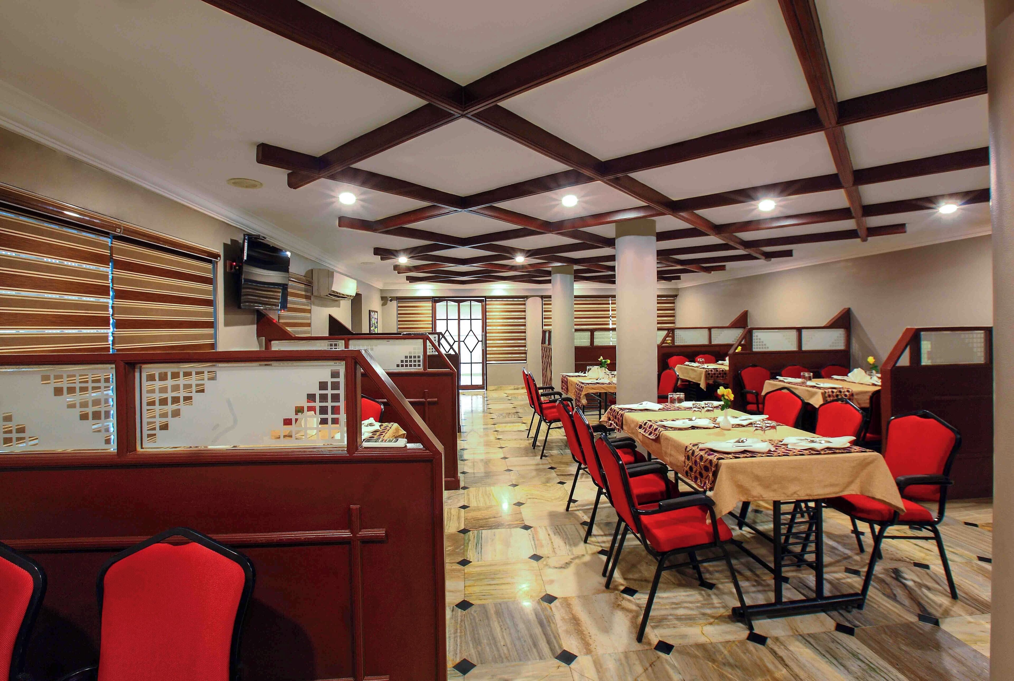 Un restaurant avec de hauts plafonds, des poutres en bois et des chaises rouges. Les tables sont dressées avec des nappes blanches et décorées de centres de table.