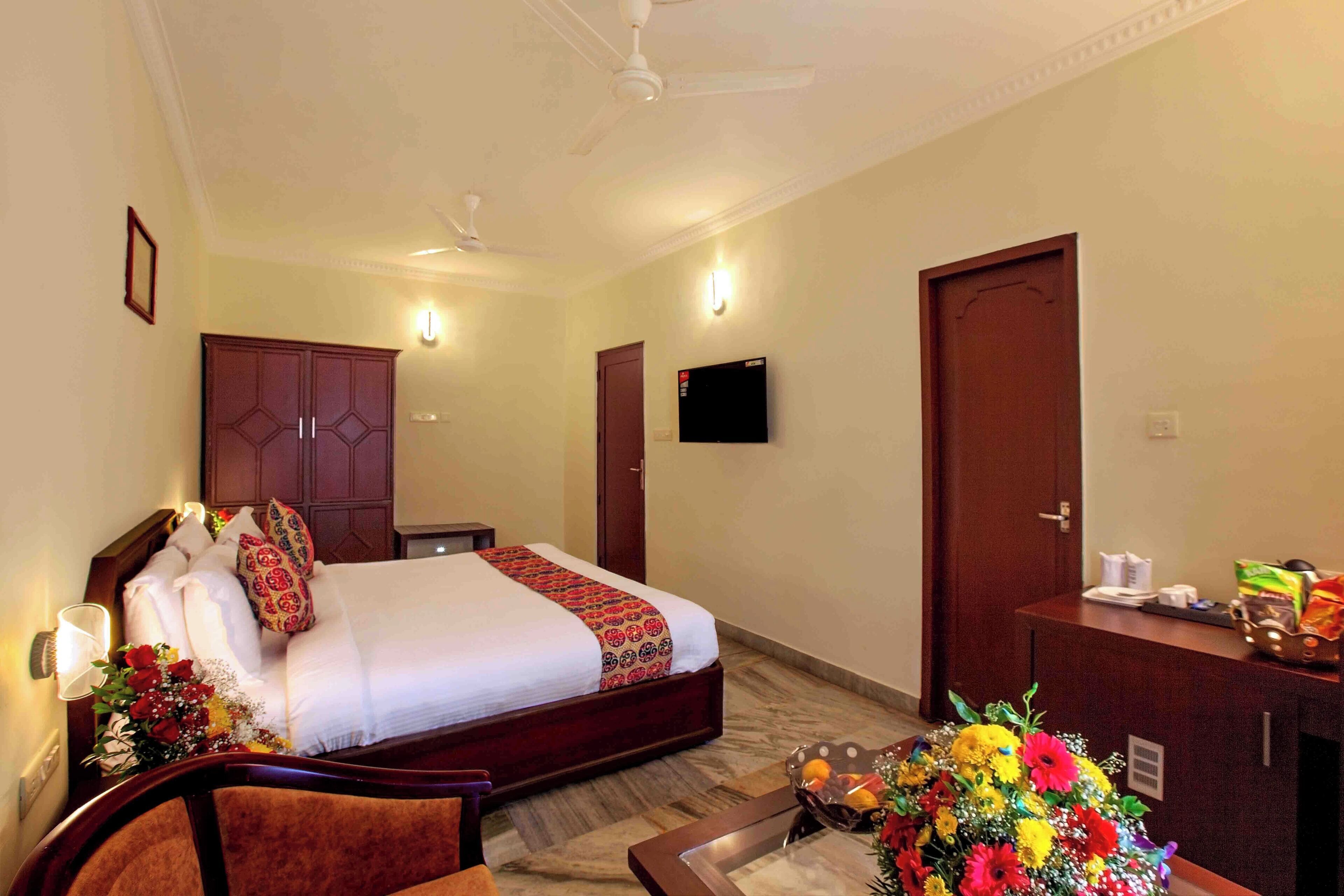 A hotel room with a bed, a desk, a chair, a TV, and a door.