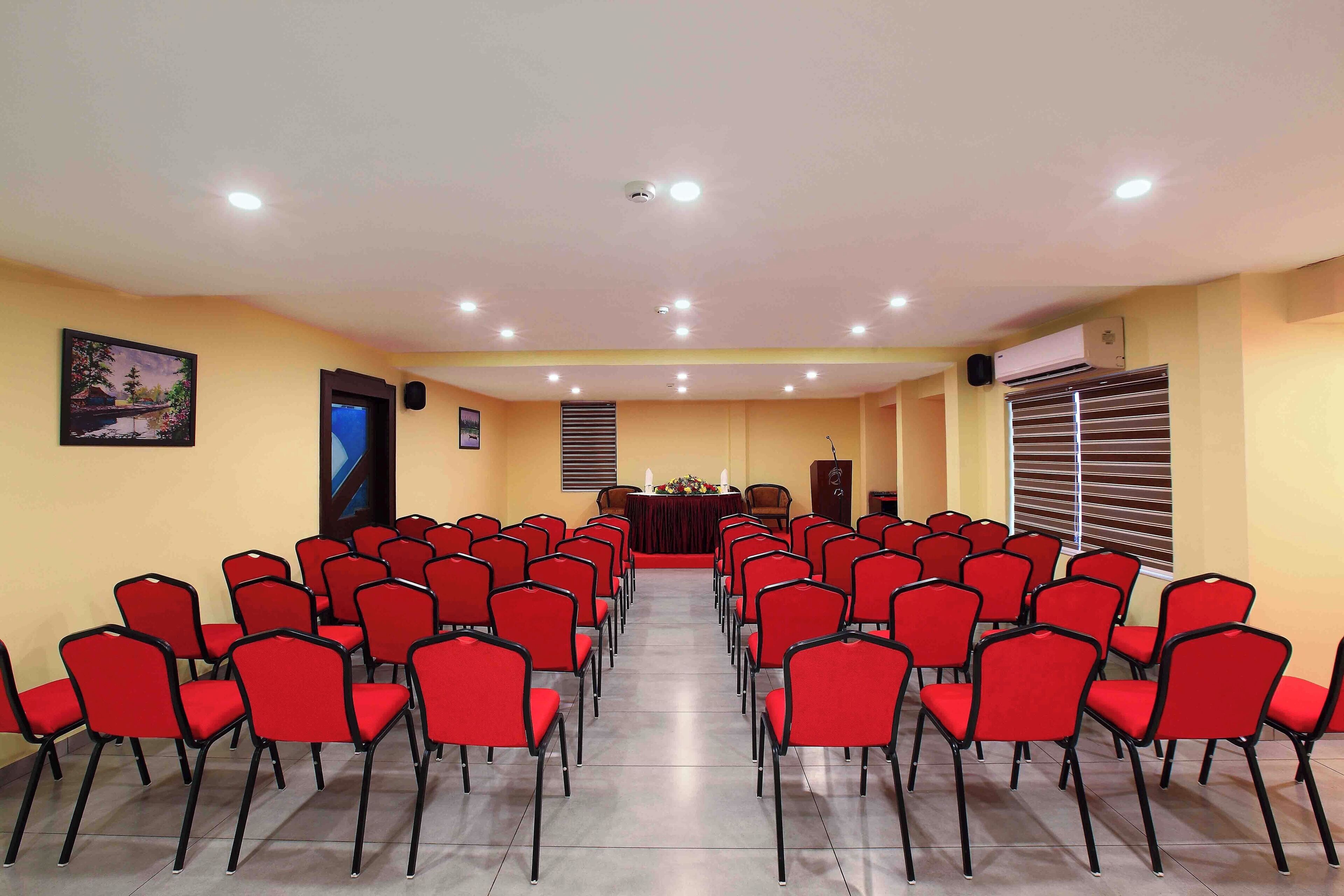 A conference room with rows of red chairs facing a stage with a podium.