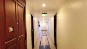 Un couloir d’hôtel avec des portes en bois, la chambre numéro 208, et un sol carrelé surmonté d’un paillasson noir et rouge.