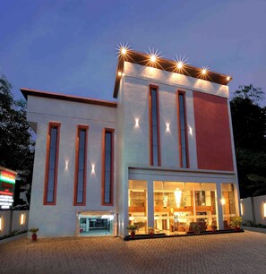 Stylish hotel building with a flat roof and modern design, featuring a glass entrance and lush greenery.