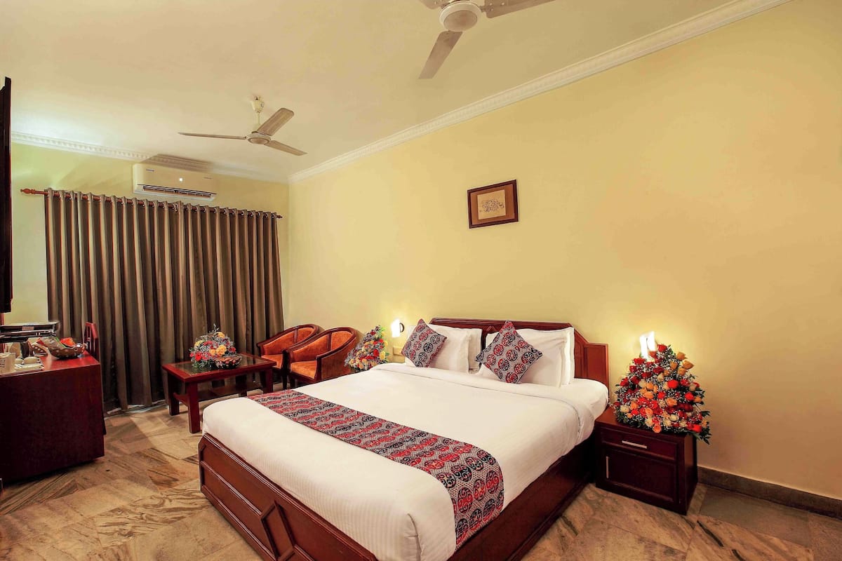 Une chambre d’hôtel comprenant un lit, un bureau, une chaise, une table de chevet avec une lampe et un ventilateur de plafond.