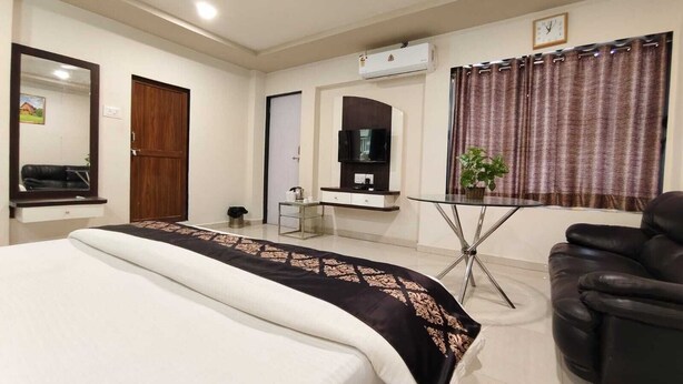 A hotel room with a bed, a TV, a desk, a chair, and an air conditioning unit.