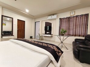 A hotel room with a bed, a TV, a desk, a chair, and an air conditioning unit.