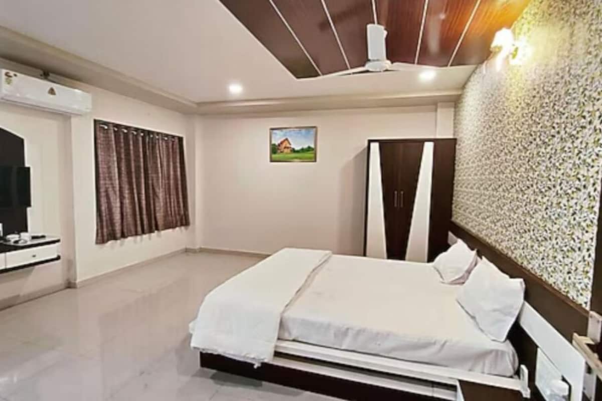 Quarto com cama, guarda-roupa, televisão e ar-condicionado fixado na parede.