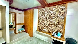 A room with a wooden wardrobe, a blue chair, a window with a decorative leaf pattern, and a small table with a kettle and cups. - Hotel Tulsi Inn (Rajula)